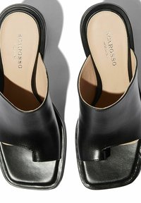 Crne kožne natikače s kvadratnim vrhom i otvorenim leđima. Glatka tekstura s suptilnim sjajem, s izrezanim detaljem na vrhu.