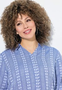 Camicia blu con bottoni, caratterizzata da un delicato motivo a righe e ricami floreali bianchi, con scollatura a V e design morbido.