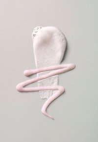 Sostanza spumosa rosa chiaro a forma di vortice astratto su uno sfondo grigio pallido, con un piccolo dettaglio a bolle nella parte superiore.