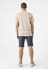 Camiseta de algodón beige combinada con pantalones cortos azul marino, con un diseño sencillo. Los pantalones cortos tienen un dobladillo enrollado y el conjunto se complementa con zapatillas claras.