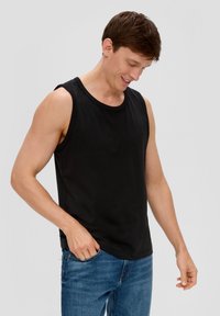 Schwarzes ärmelloses Tanktop aus Baumwolle mit Rundhalsausschnitt und lässiger Passform, kombiniert mit blauen Jeans.