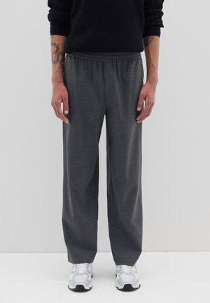 Graue, weit geschnittene Hosen aus weichem Stoff mit elastischem Bund. Sie haben eine glatte Textur und sind mit weißen Sportschuhen kombiniert.