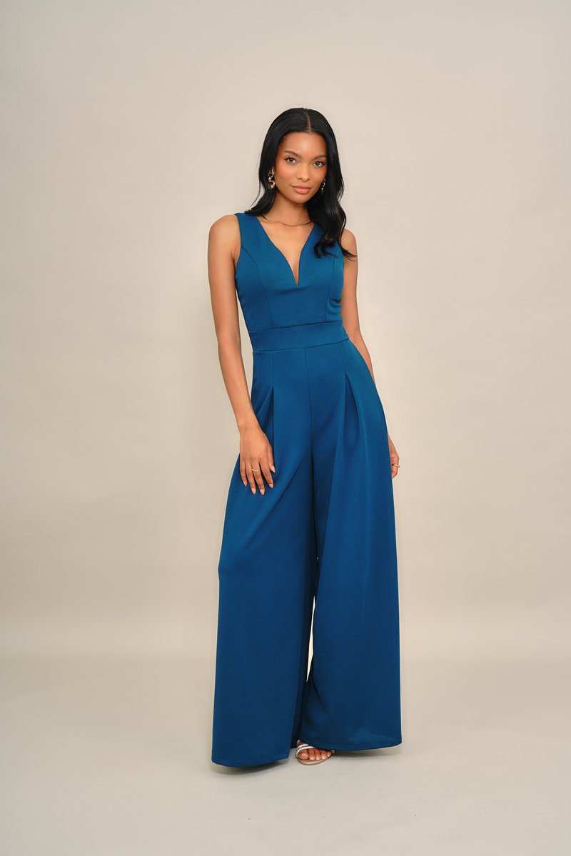 Türkizkék overall mélyen dekoltált nyakkivágással, ujjatlan kialakítással, széles szárakkal, redős részletekkel, sima anyagból készült.