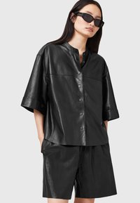 Black leather shirt with a round collar, short sleeves, and button front. Paired with black leather shorts, both feature a smooth texture.