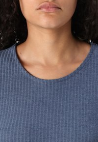 Blå ribbad textil med rund halsringning, med en subtil textur. Övre torso vy fokuserar på tyg och design detaljer.