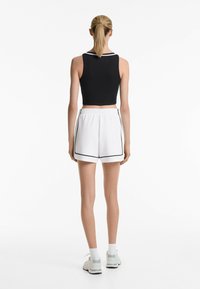 Sort cropped tanktop med en hvid halskant, parret med hvide atletikshorts med sorte sideaksenter og et elastisk liv. 