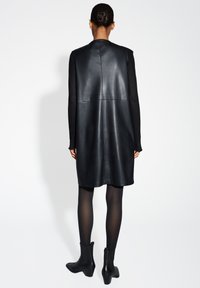 Zwarte leren jurk met een aansluitende bustier, A-lijnvorm en naaddetails. Gedirigeerd met zwarte enkellaarzen en doorschijnende zwarte panty's.