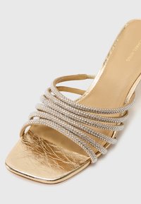 Sandale à talon haut dorée à bout ouvert avec cinq brides étincelantes en strass sur le devant et un design à bout carré.