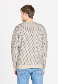 Lichtbeige trui met zwarte driehoekige patronen, geribbelde manchetten en zoom, ronde halslijn en gebreide textuur. Draag met blauwe jeans.