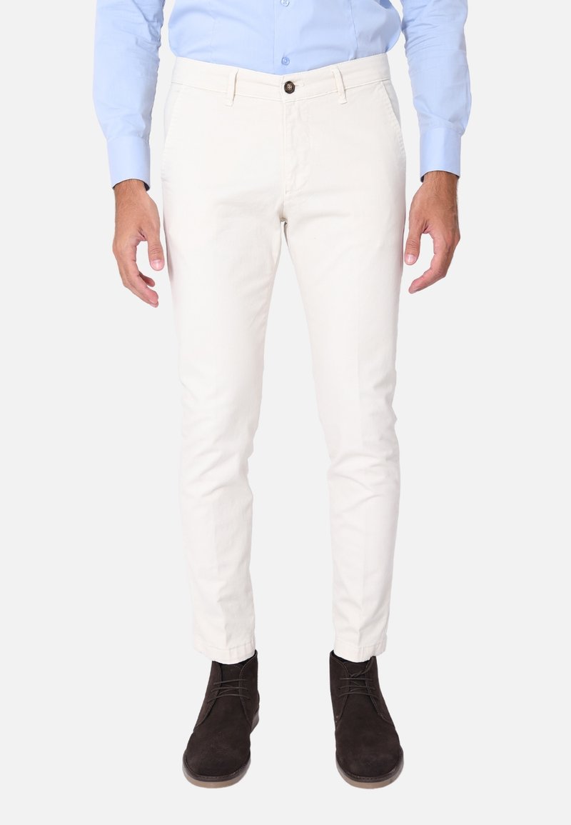 Chinos bianchi in cotone con vestibilità slim, dotati di chiusura con bottone frontale e tasche. Abbinati a stivali in suede marrone scuro.
