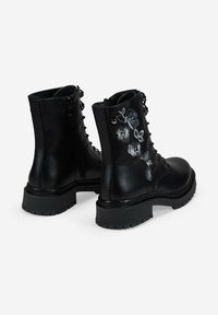 Botas de cuero negro con cordones, cremalleras laterales, suelas gruesas acanaladas y diseños florales bordados en plata en los laterales exteriores.