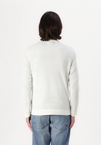 Suéter de manga larga en gris claro, hecho de material suave. Cuenta con un escote redondo y puños de canalé, combinado con jeans azules de corte holgado.