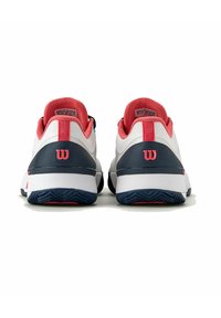 Zapatillas deportivas blancas con acentos rojos y detalles en azul marino. Parte superior de tejido texturizado, cuello acolchado y suela de goma con patrón. Logo de Wilson destacado.