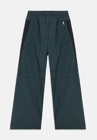 Breda byxor i mörk teal-tyg med en texturerad yta, med svarta sidpaneler och en zippered ficka på högra sidan.