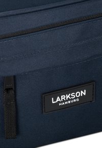 Borsa in tessuto blu navy con superficie testurizzata. Presenta un'etichetta nera prominente con testo bianco "LARKSON HAMBURG" e un dettaglio con zip.