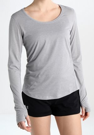 Vrouw draagt een grijs langarmshirt met duimgaten en zwarte sportkorte broek tegen een effen achtergrond.