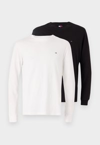 Langärmlige T-Shirts aus weißer und schwarzer Baumwolle, mit einem kleinen farbigen Logo auf der linken Brust, abgerundetem Halsausschnitt und umgeschlagenen Ärmeln.