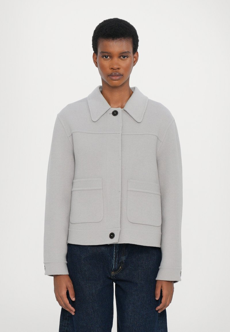 Light grey jacket made of soft fabric, featuring a spread collar, two front pockets, a front button closure, and long sleeves.