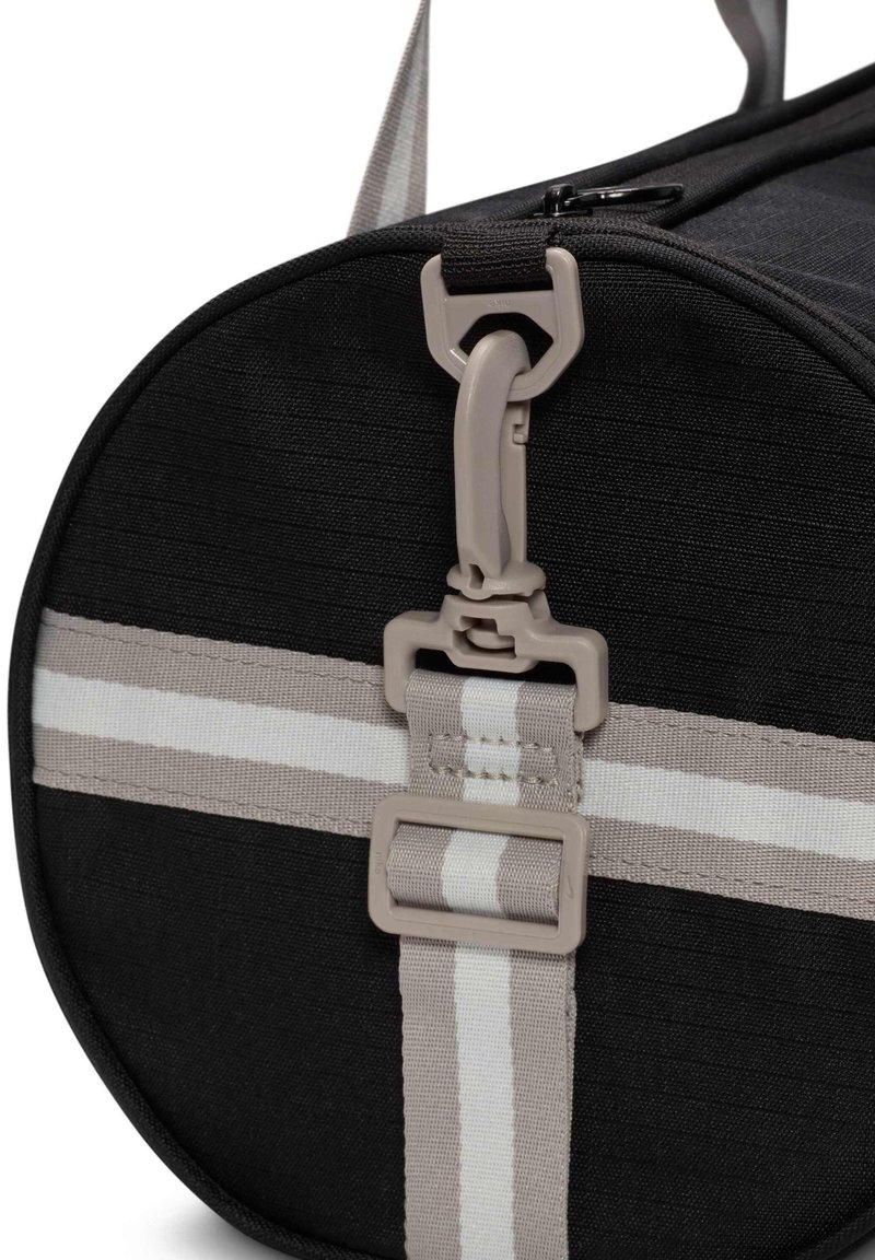 Bolsa cilíndrica negra con una superficie texturizada, que cuenta con una correa gris con rayas blancas y un detalle de hebilla de hardware gris.