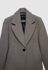 Cappotto di lana grigio con ampio colletto a revers, chiusura con un bottone, due tasche frontali e foderato in morbido nero. Etichetta di taglia S visibile.