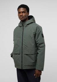 Green, hooded jacket with a front zipper, two large front pockets, and a smooth, matte texture. Features an accent patch on the sleeve.