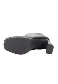 Bota de cuero negro con un upper liso, punta redondeada y un robusto tacón de bloque. Suela de goma texturizada con ranuras horizontales para un mejor agarre.