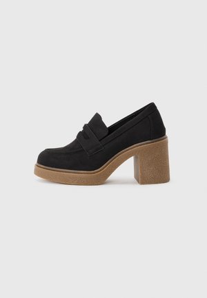 Black suede loafers with a thick, textured tan heel. Features a subtle front strap detail. Rounded toe design with smooth edges.