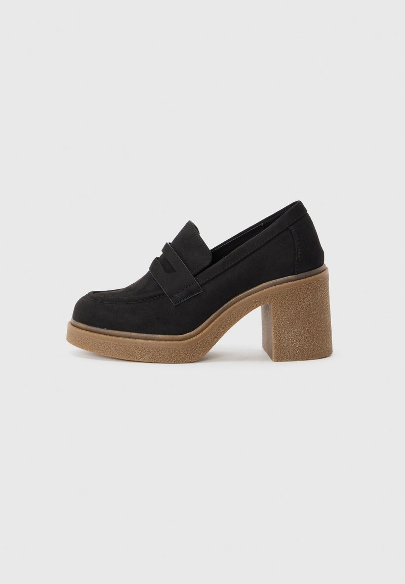 Mocassins en suède noir avec un talon large et texturé de couleur tan. Présente un détail subtil de sangle à l'avant. Design à bout rond avec des bords lisses.