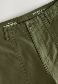 Pantalons vert olive en tissu mélange de coton, présentant une coupe régulière, une fermeture à bouton et des accents cousus. Taille 34 R indiquée.