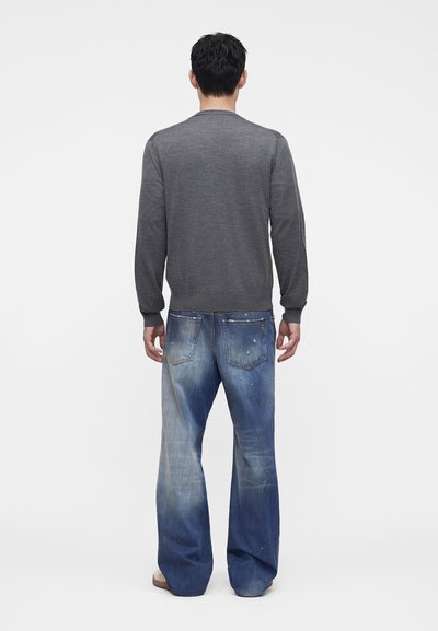 Homme debout de dos portant un t-shirt gris à manches longues et un jean bleu délavé ample avec des éclaboussures de peinture.