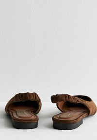 Bruine suède instapschoenen met een geplooide achterkant, een vlakke zwarte zool en een gevormde voetbed, met een soepele binnenvoering en een minimalistisch ontwerp.