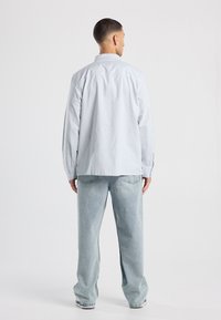 Camicia a righe azzurra con vestibilità rilassata, maniche lunghe e dettagli con bottoni, abbinata a jeans a gamba larga chiari.