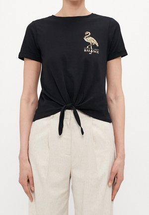 Czarny t-shirt z krótkim rękawem z węzłem na wysokości talii, z grafiką złotego flaminga i napisem "W ŻYCIU CHODZI O RÓWNOWAGĘ."