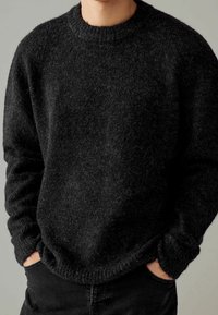 Maglione nero a maglia con finitura texturizzata, collo a giro e polsini a coste. Presenta una vestibilità rilassata e un aspetto peloso.
