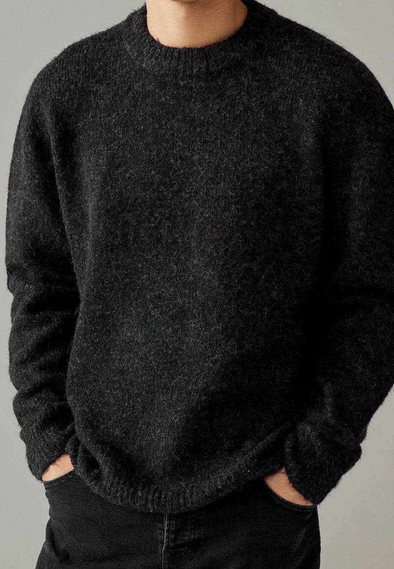 Maglione nero a maglia con finitura texturizzata, collo a giro e polsini a coste. Presenta una vestibilità rilassata e un aspetto peloso.