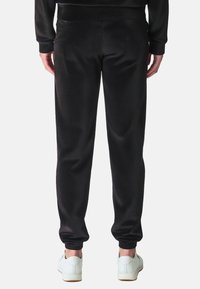 Zwarte sportieve sweatpants van een gladde stof, met een elastische tailleband en taps toelopende boorden, gedragen met witte sneakers. Geen zichtbare patronen of logo's.