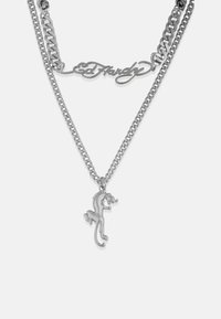 Ασημένιο μέταλλο κολιέ με διπλές αλυσίδες. Μια αλυσίδα έχει ένα καλλιγραφικό πε pendant "Ed Hardy" με ένα λεπτομερές charm ζώου που πηδά.
