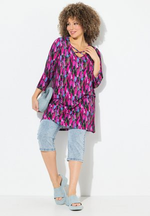 Tunic colorata con sfondo nero, caratterizzata da motivi astratti rosa e blu, abbinata a jeans capri azzurri e sandali con zeppa.