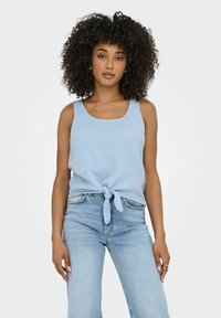 Ljusblå, ärmlös tanktop med en knuten framdetalj, gjord av strukturerad tyg, kombinerad med ljusa denimjeans.