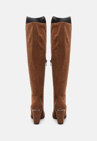 Bottes hautes en daim marron jusqu'au-dessus du genou avec une texture lisse, dotées d'un talon bloc, d'une fermeture éclair et d'une doublure noire contrastante.
