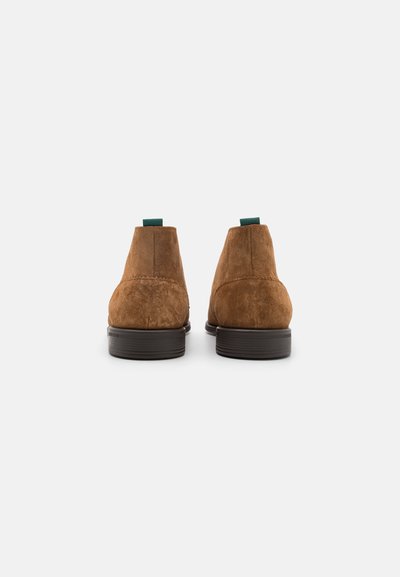 Bruine suède enkellaarsjes met een gevormde hak, voorzien van een groene lus aan de achterkant voor eenvoudig aan- en uittrekken. Glad textuur en minimalistich ontwerp.