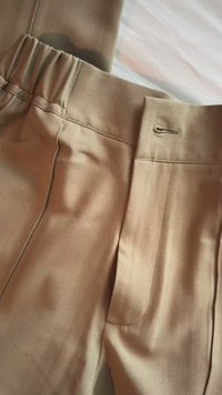 Pantaloni beige con una cintura elastica e un asola sul davanti, che evidenziano la texture del tessuto e i dettagli delle cuciture.