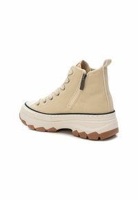 Zapatilla alta beige de ante con una cremallera lateral, cordones beige y una suela de goma blanca gruesa con acentos marrones.