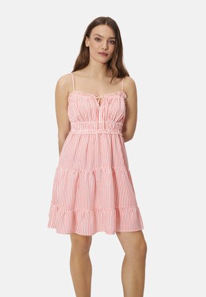 Mujer de pie con vestido sin mangas de rayas verticales rosas y blancas, con bajo con volantes y tirantes finos, sobre fondo liso.