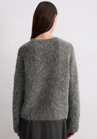 Grijze, fluffy gebreide trui met een losse pasvorm, brede ronde halslijn en lange mouwen; textuur materiaal en een iets cropped zoom.