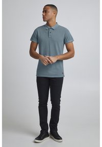 Lys blå polo-shirt med korte ærmer, to knapper, slim fit. Kombineret med mørke slim-fit jeans og sorte sneakers med hvide såler.