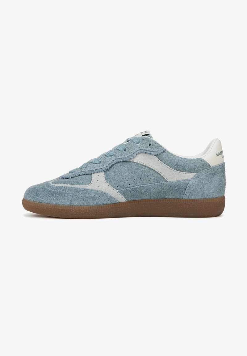 Blauwe suède sneaker met witte accenten, gestructureerd oppervlak, geperforeerde zijkanten, platte bruine rubberen zool en vetersysteem. Minimale branding op de hiel.