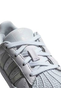 Baskets en cuir blanc avec des rayures perforées sur les côtés, lacets plats blancs et semelle en caoutchouc texturée. Dotées d'un logo en relief sur la languette.