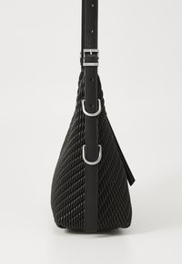 Μαύρη υφασμένη δερμάτινη τσάντα με καμπύλο τριγωνικό σχήμα, διαθέτει ασημένιο κούμπωμα και μεταλλικά στοιχεία. Απαλή υφή και ρυθμιζόμενος ιμάντας.