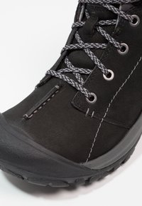 Bota de senderismo negra con parte superior sintética, superficie texturada, cordones grises y puntera de goma reforzada para mayor durabilidad y soporte.